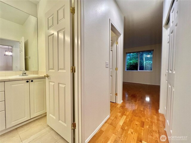 hallway featuring a sink, baseboards, and light wood-style floors