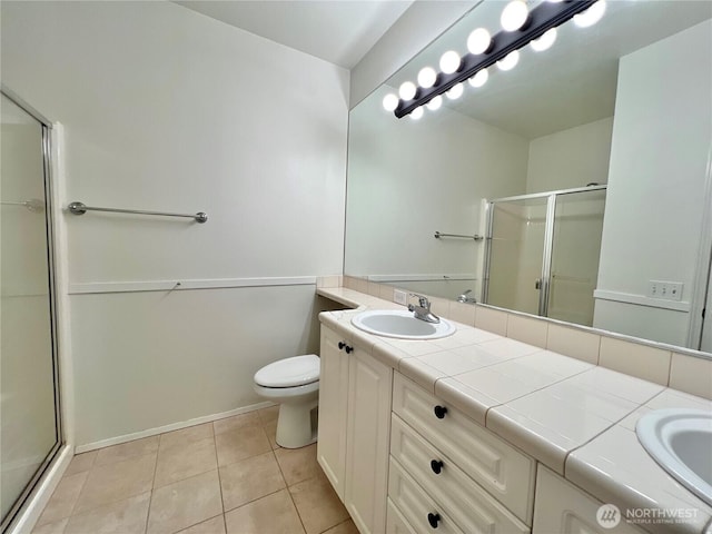 bathroom featuring tile patterned floors, a shower stall, double vanity, toilet, and a sink
