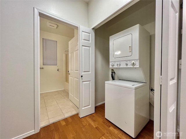 laundry area featuring stacked washer / dryer, light wood-style flooring, laundry area, and baseboards