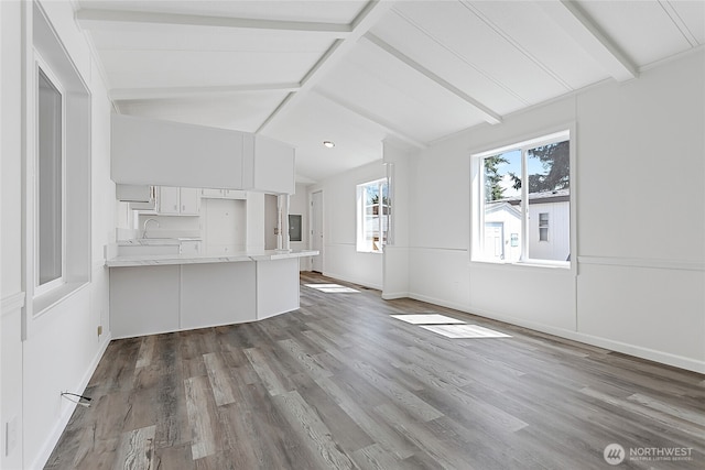 unfurnished living room with baseboards, lofted ceiling with beams, a sink, and wood finished floors