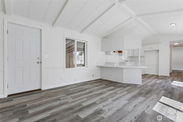 kitchen featuring a sink, a peninsula, lofted ceiling with beams, light countertops, and white cabinets