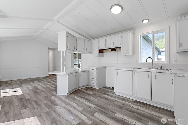 kitchen featuring light wood-style flooring, a sink, light countertops, white cabinets, and vaulted ceiling with beams