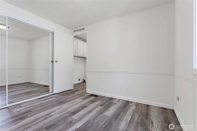 unfurnished bedroom with a closet, visible vents, wood finished floors, and baseboards