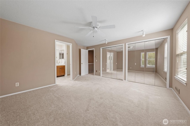 unfurnished bedroom featuring visible vents, baseboards, two closets, connected bathroom, and light carpet