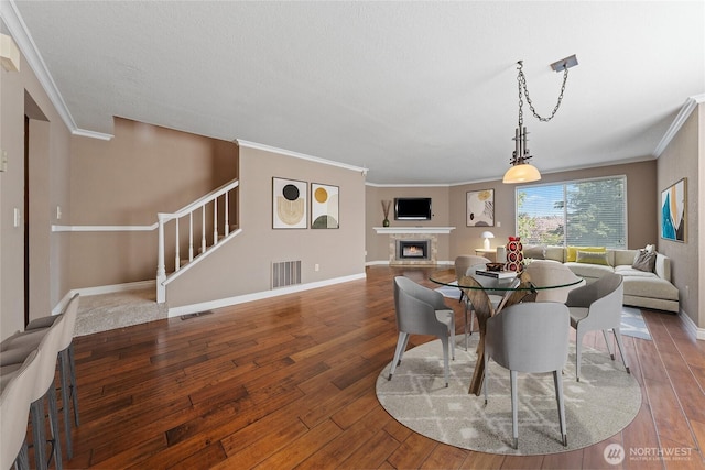 dining space with visible vents, crown molding, a warm lit fireplace, and hardwood / wood-style flooring