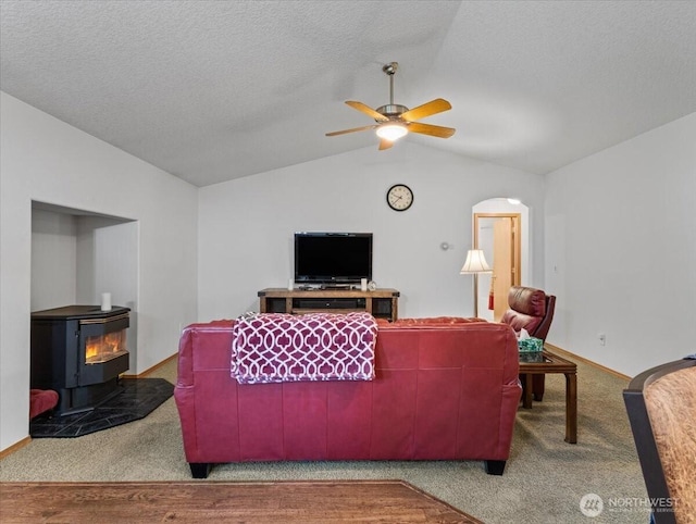 carpeted living area featuring baseboards, a wood stove, a ceiling fan, a textured ceiling, and lofted ceiling