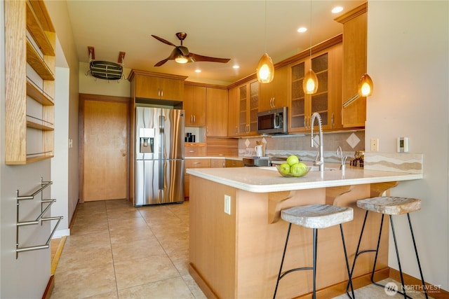 kitchen featuring brown cabinets, appliances with stainless steel finishes, a peninsula, a ceiling fan, and tasteful backsplash