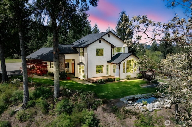back of property at dusk with a lawn and a shingled roof
