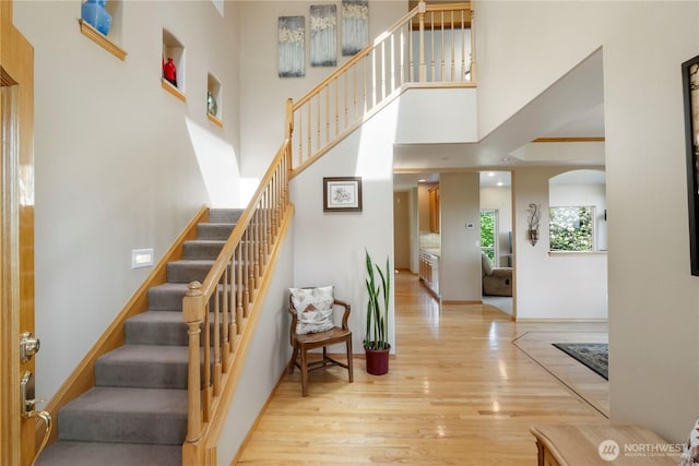 stairway featuring arched walkways, wood finished floors, and a towering ceiling