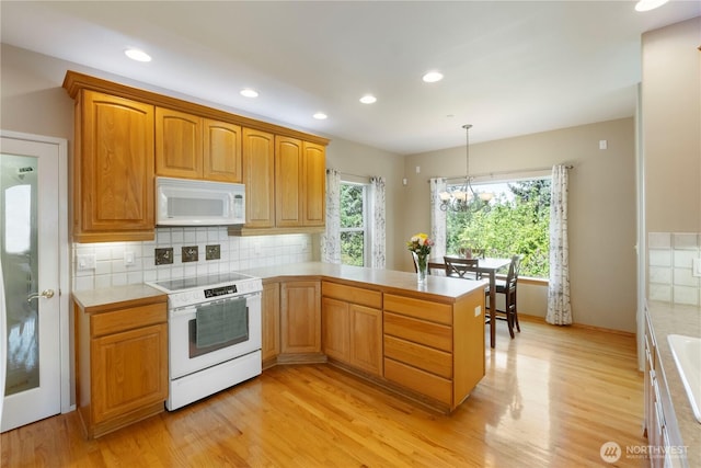 kitchen featuring light countertops, a peninsula, white appliances, and light wood-style flooring