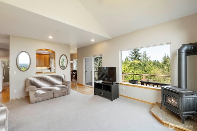 carpeted living area featuring arched walkways, a wood stove, vaulted ceiling, baseboards, and recessed lighting