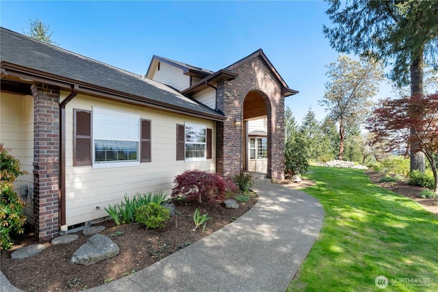 view of front of house featuring a shingled roof, a front yard, and brick siding