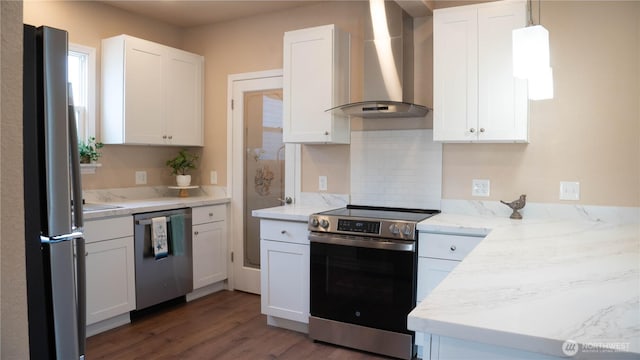 kitchen with light stone countertops, stainless steel appliances, wall chimney range hood, white cabinets, and wood finished floors