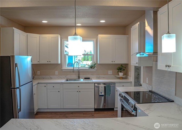 kitchen with light stone countertops, a sink, stainless steel appliances, wall chimney range hood, and white cabinets