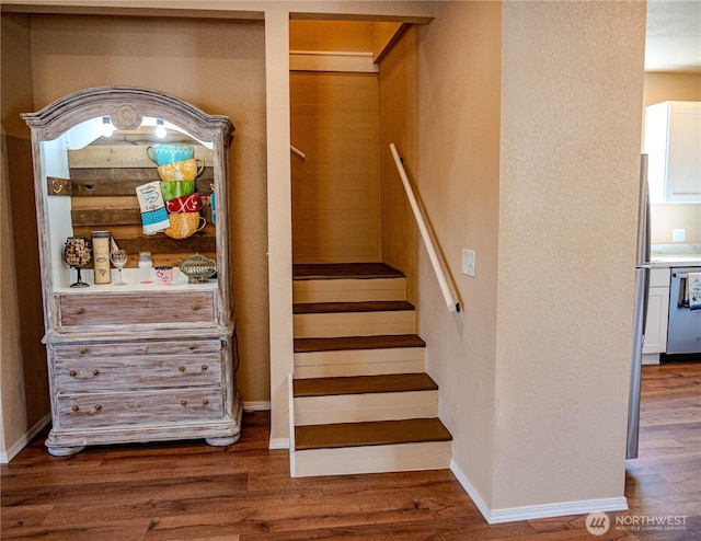 staircase featuring baseboards, wood finished floors, and a textured wall