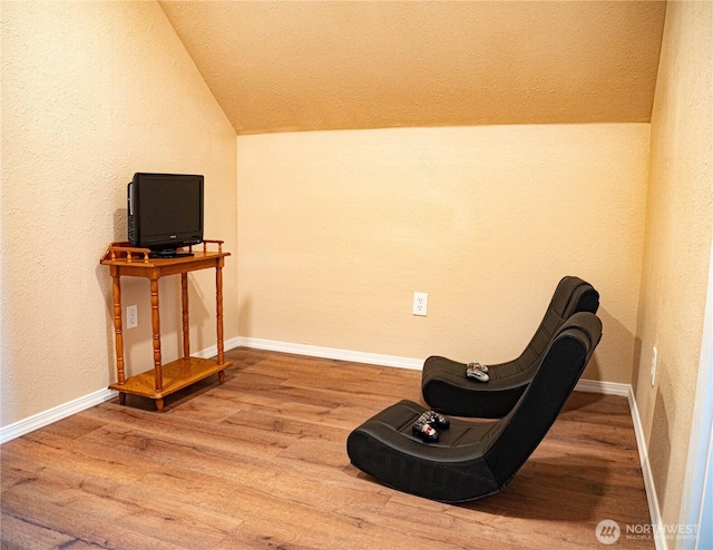 living area with baseboards, wood finished floors, lofted ceiling, and a textured wall