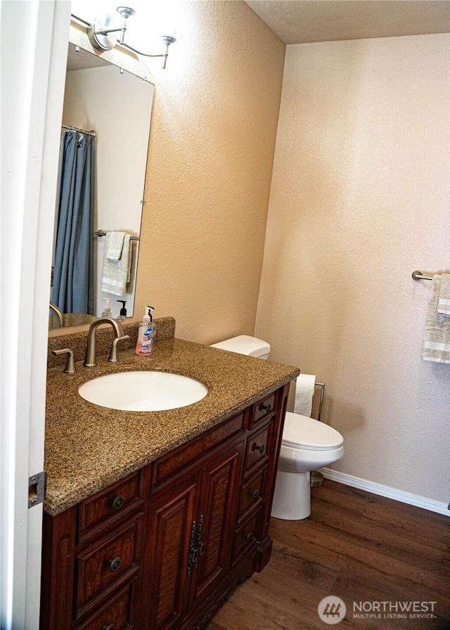 full bathroom with vanity, toilet, a textured wall, baseboards, and wood finished floors
