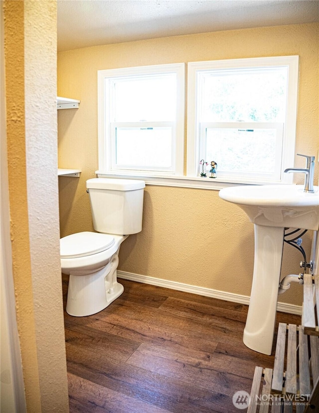half bathroom featuring baseboards, wood finished floors, toilet, and a textured wall