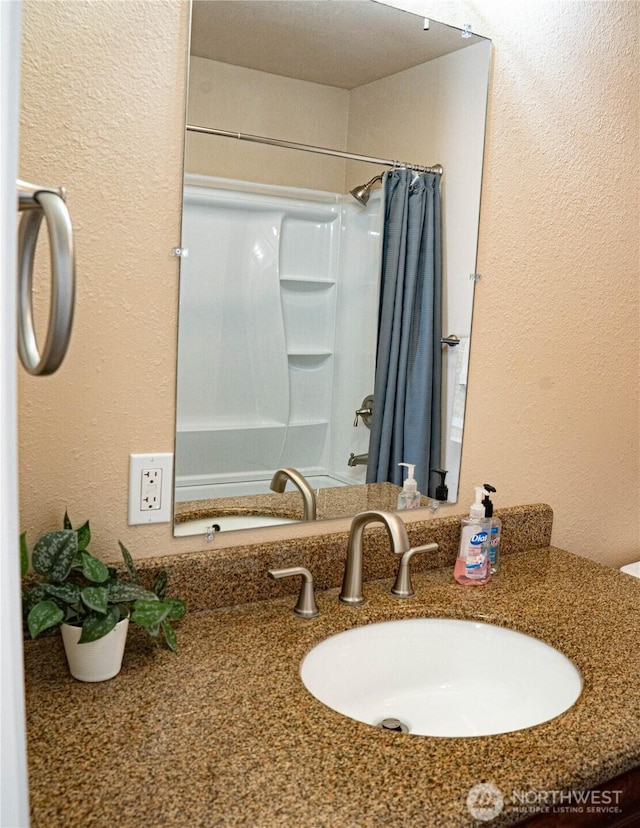 bathroom featuring shower / tub combo with curtain, a textured wall, and vanity