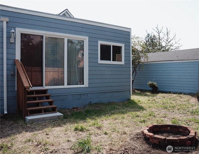 view of property exterior with a lawn, a fire pit, and entry steps