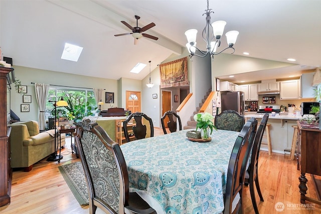 dining room with a ceiling fan, light wood-style flooring, stairs, beamed ceiling, and a skylight