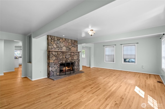 unfurnished living room with baseboards, wood finished floors, a stone fireplace, and beam ceiling