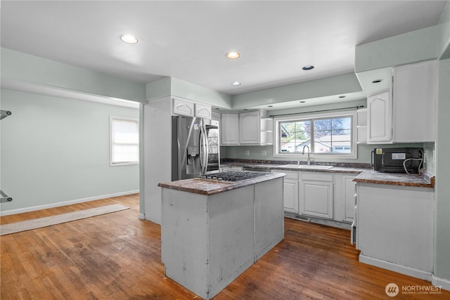 kitchen with white cabinets, a sink, appliances with stainless steel finishes, a kitchen island, and dark wood-style flooring