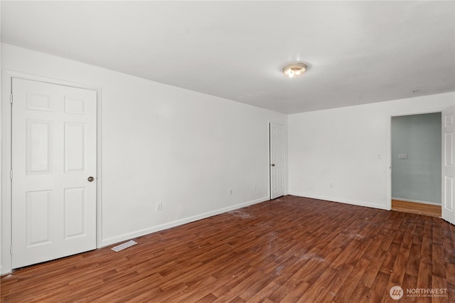 spare room with baseboards, visible vents, and wood finished floors