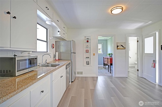 kitchen with a sink, light wood-style flooring, stainless steel appliances, white cabinetry, and visible vents