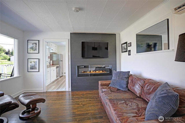 living area with a large fireplace, a wall unit AC, and wood finished floors
