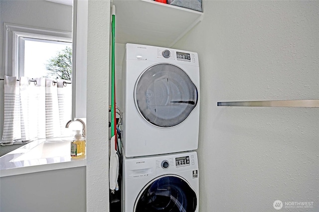washroom featuring stacked washing maching and dryer, a textured wall, and laundry area