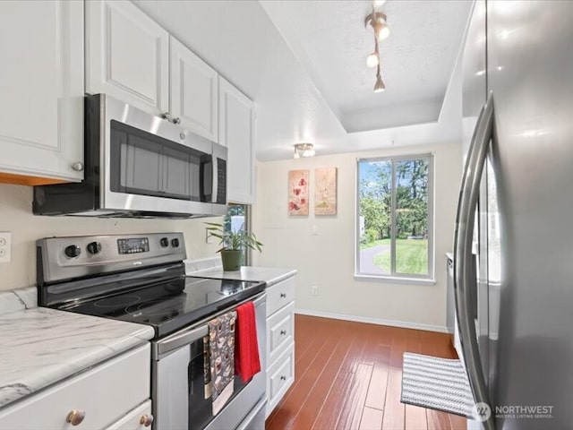 kitchen featuring appliances with stainless steel finishes, white cabinetry, baseboards, dark wood-type flooring, and a tray ceiling