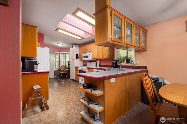 kitchen featuring tile countertops, a sink, a peninsula, and white appliances