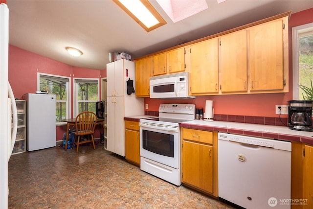 kitchen with white appliances, tile countertops, tile patterned floors, and vaulted ceiling