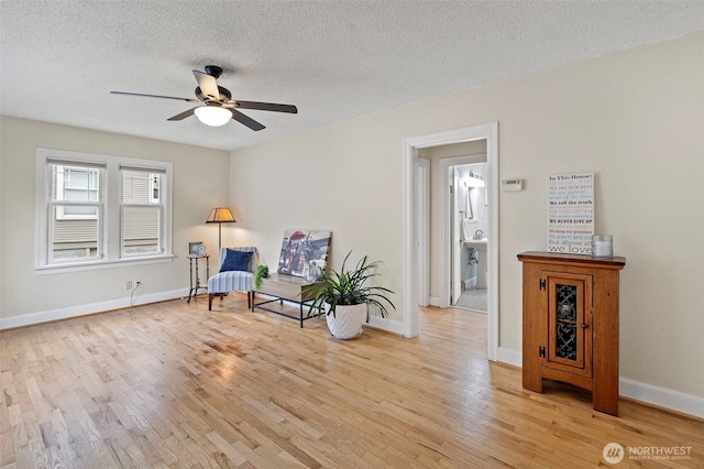 living area with a textured ceiling, baseboards, a ceiling fan, and light wood-style flooring