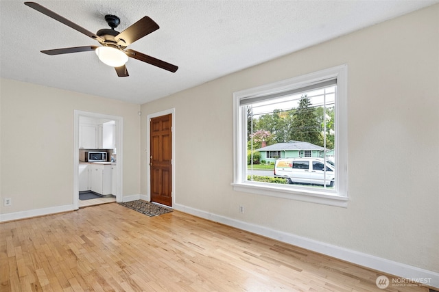 interior space with a textured ceiling, ceiling fan, baseboards, and light wood-type flooring