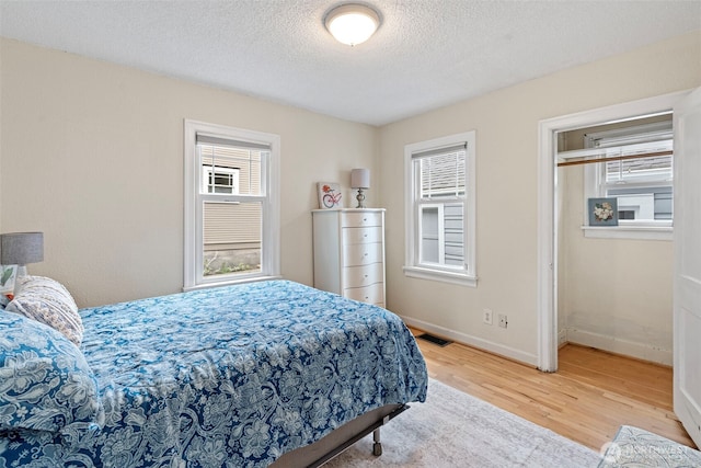 bedroom featuring a textured ceiling, baseboards, wood finished floors, and visible vents
