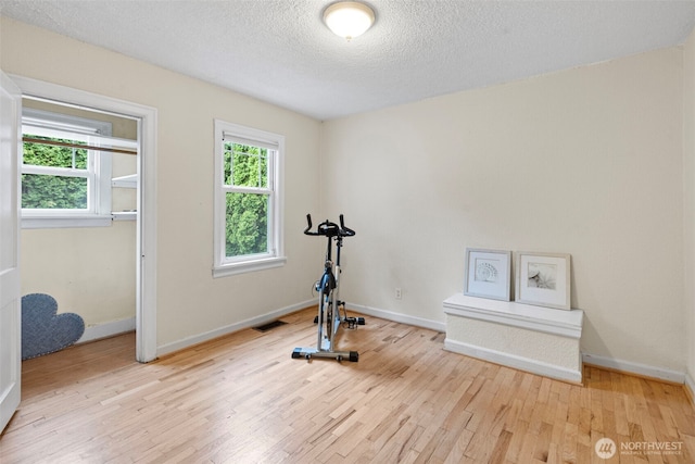 workout area with baseboards, a textured ceiling, visible vents, and wood finished floors