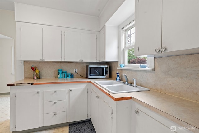 kitchen featuring decorative backsplash, light countertops, stainless steel microwave, white cabinets, and a sink