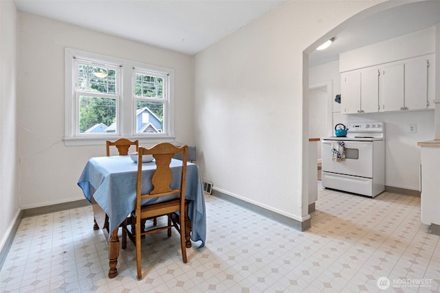 dining area featuring arched walkways, baseboards, and light floors