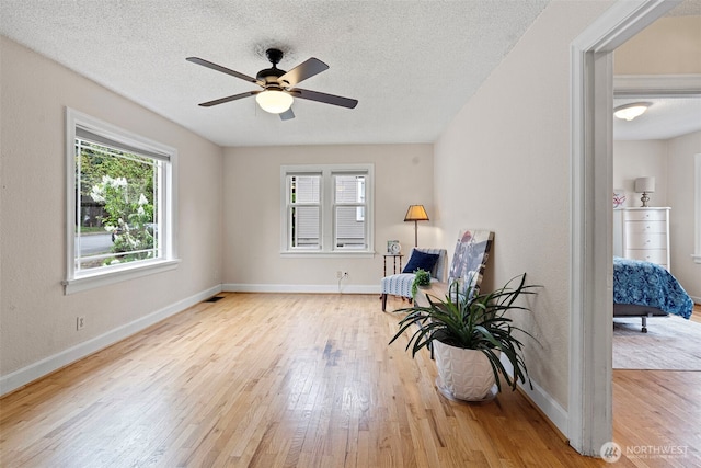 living area with baseboards, ceiling fan, a textured ceiling, and wood finished floors
