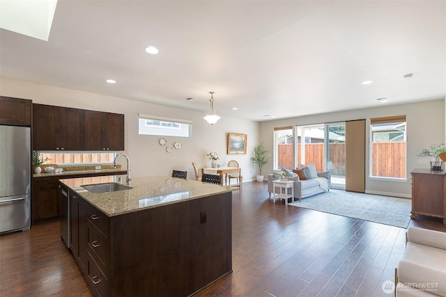 kitchen with dark wood-style flooring, light stone counters, stainless steel refrigerator, and a sink