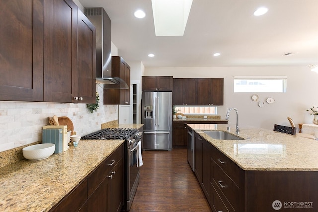 kitchen featuring a kitchen island with sink, tasteful backsplash, light stone counters, a sink, and appliances with stainless steel finishes