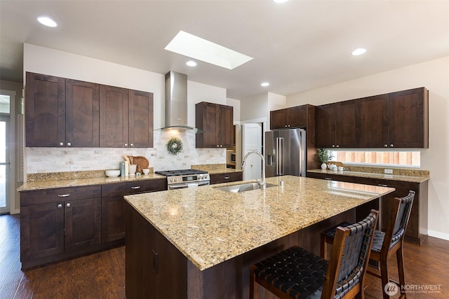 kitchen featuring wall chimney range hood, a breakfast bar area, a skylight, appliances with stainless steel finishes, and a sink