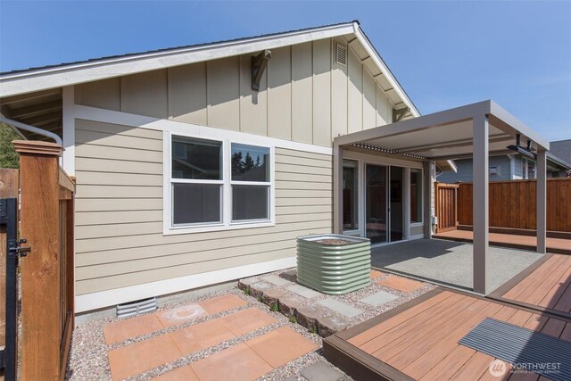 rear view of house with fence, a wooden deck, a patio area, board and batten siding, and crawl space