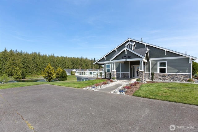 view of front of house featuring driveway, stone siding, and a front yard