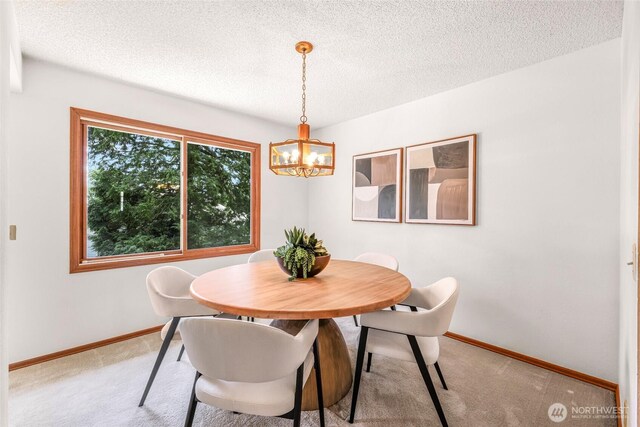 dining room featuring light colored carpet, a textured ceiling, baseboards, and a notable chandelier