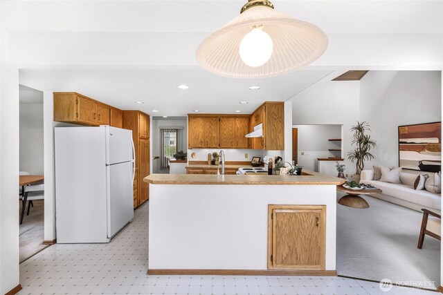 kitchen featuring brown cabinets, light countertops, freestanding refrigerator, a peninsula, and under cabinet range hood