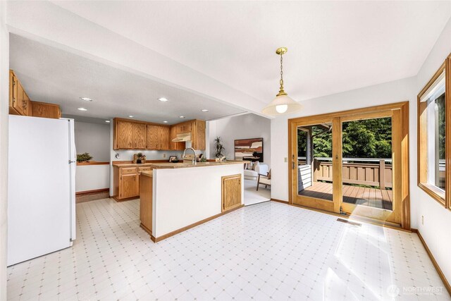 kitchen featuring light countertops, freestanding refrigerator, a peninsula, light floors, and under cabinet range hood