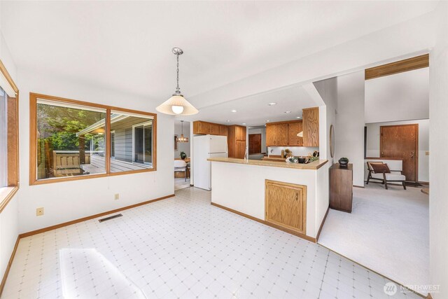 kitchen featuring visible vents, pendant lighting, freestanding refrigerator, a peninsula, and light carpet